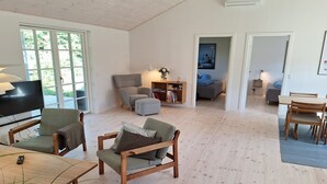 Un salón amplio con televisor, asientos y una estantería.