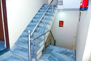 A marble staircase with metal railings, a fire extinguisher, and a small decorative item on the wall. - Hotel Relax (Jaipur)