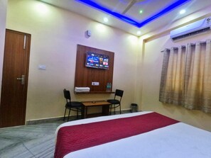 A hotel room with a bed, a TV mounted on the wall, a small table with two chairs, and a curtain on the window. - Hotel Relax (Jaipur)