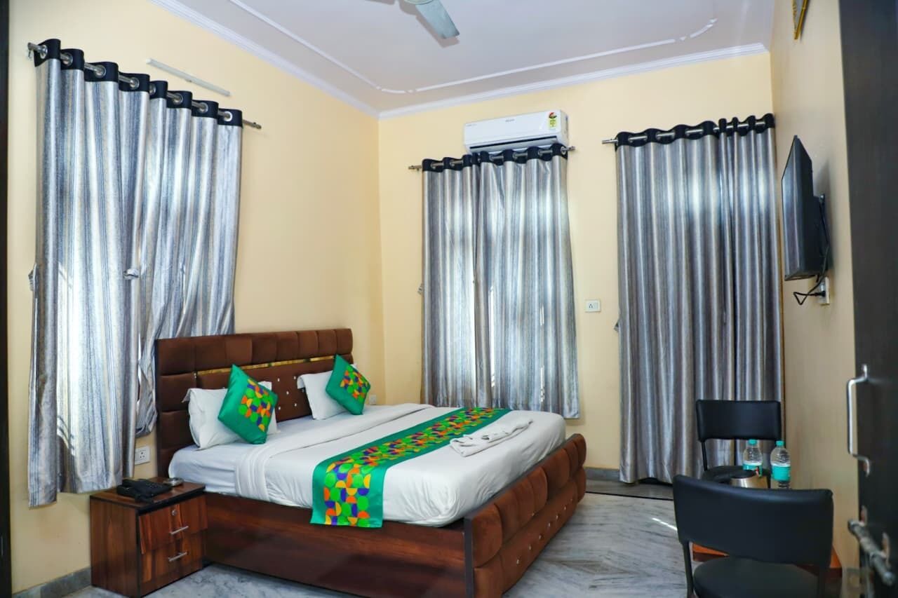 A hotel room with a bed, curtains, a television, and a desk with a chair.