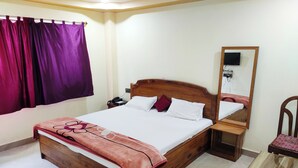 A neatly made bed with a wooden headboard, a bedside table with a phone, a mirror, and a small table with a chair. - LUXURY INN  (Chakradharpur)