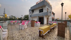 A hotel with a terrace area featuring tables and chairs, a balcony, and a building with the hotel's name. - LUXURY INN  (Chakradharpur)