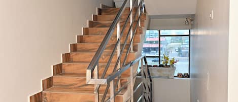 Eine Treppe mit Holzstufen und Metallgeländern, die zu einer Zwischenebene mit einem Fenster mit Blick auf eine Straße führt.