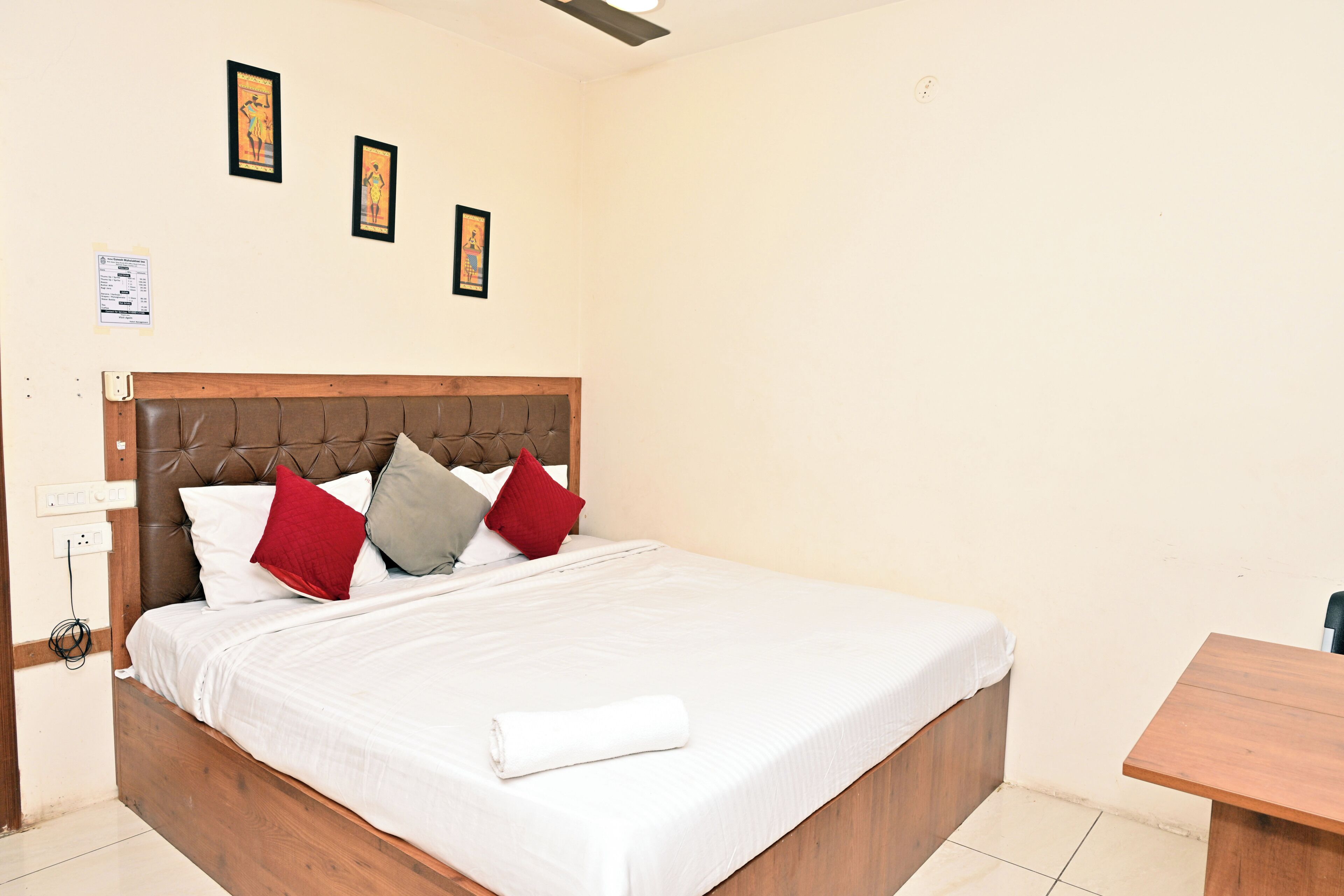 A hotel room with a wooden bed, white bedding, and three framed pictures on the wall.