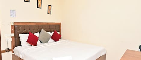 A hotel room with a wooden bed, white bedding, and three framed pictures on the wall.