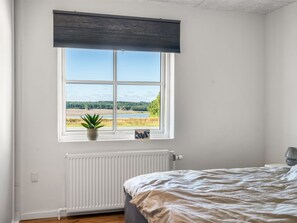 Une chambre avec une grande fenêtre, un radiateur, un lit et une plante en pot.