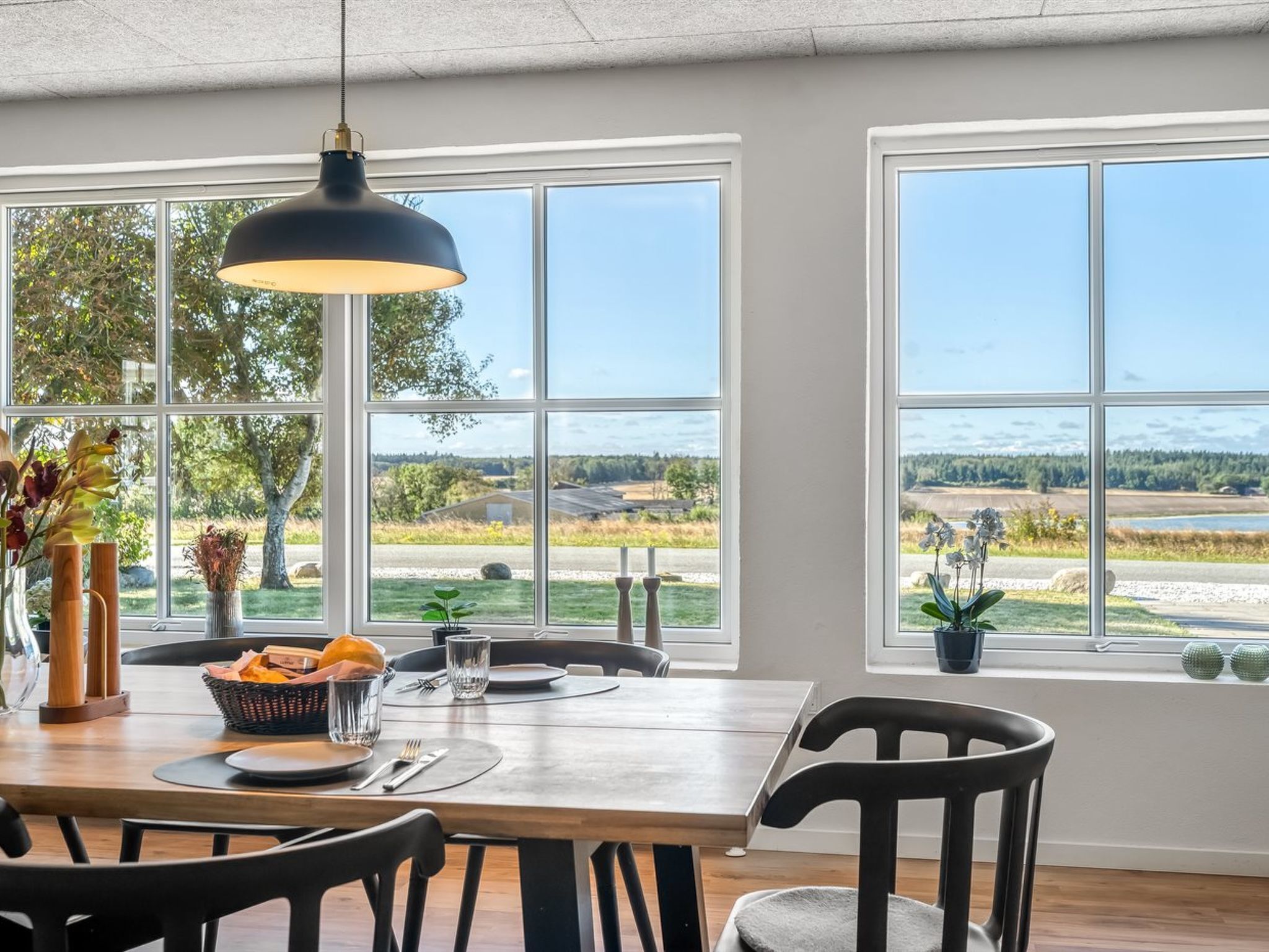A dining area with a table set for two, large windows with a view of a landscape, and a pendant light above the table.