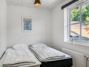 Ein kleines Zimmer mit einem Einzelbett, einem Fenster, einer Heizung und einem Bild an der Wand.