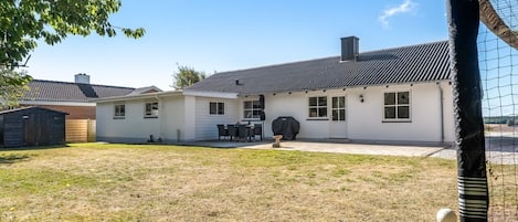 A residential backyard with a house, a barbecue area, and a fenced play area.
