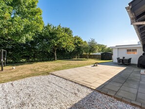 Un jardin à l’arrière d’une maison, avec une terrasse, une pelouse et un abri de jardin.