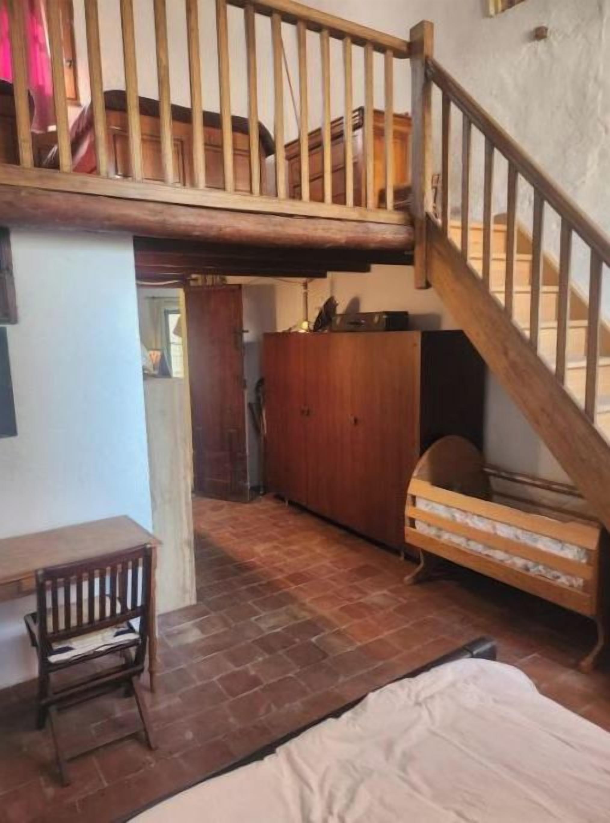 A room with a loft area, a wooden staircase, a bed, a desk, and a chair.