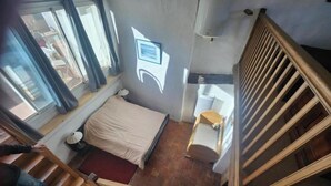 A bedroom with a bed, a bedside table, a window, and a staircase. - The Boat on the Rooftops (Cotignac)