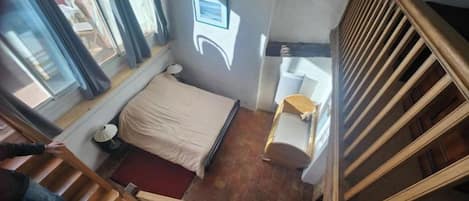 Un dormitorio con cama, mesita de noche, ventana y escalera.