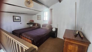 A bedroom with two beds, a wooden dresser, a hanging lamp, and a window with curtains. - The Boat on the Rooftops (Cotignac)