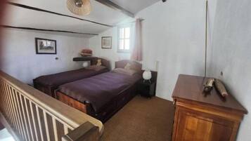 Quarto com duas camas, cômoda de madeira, luminária pendente e janela com cortinas.