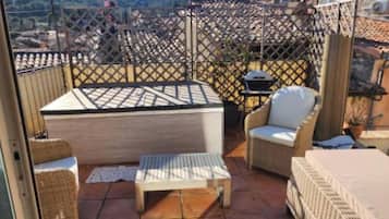 Una terrassa amb mobles de vimet, una taula i una barbacoa.
