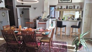 A dining area with a table set for four, surrounded by wooden chairs, a patterned rug, and a hanging light fixture. - The Boat on the Rooftops (Cotignac)