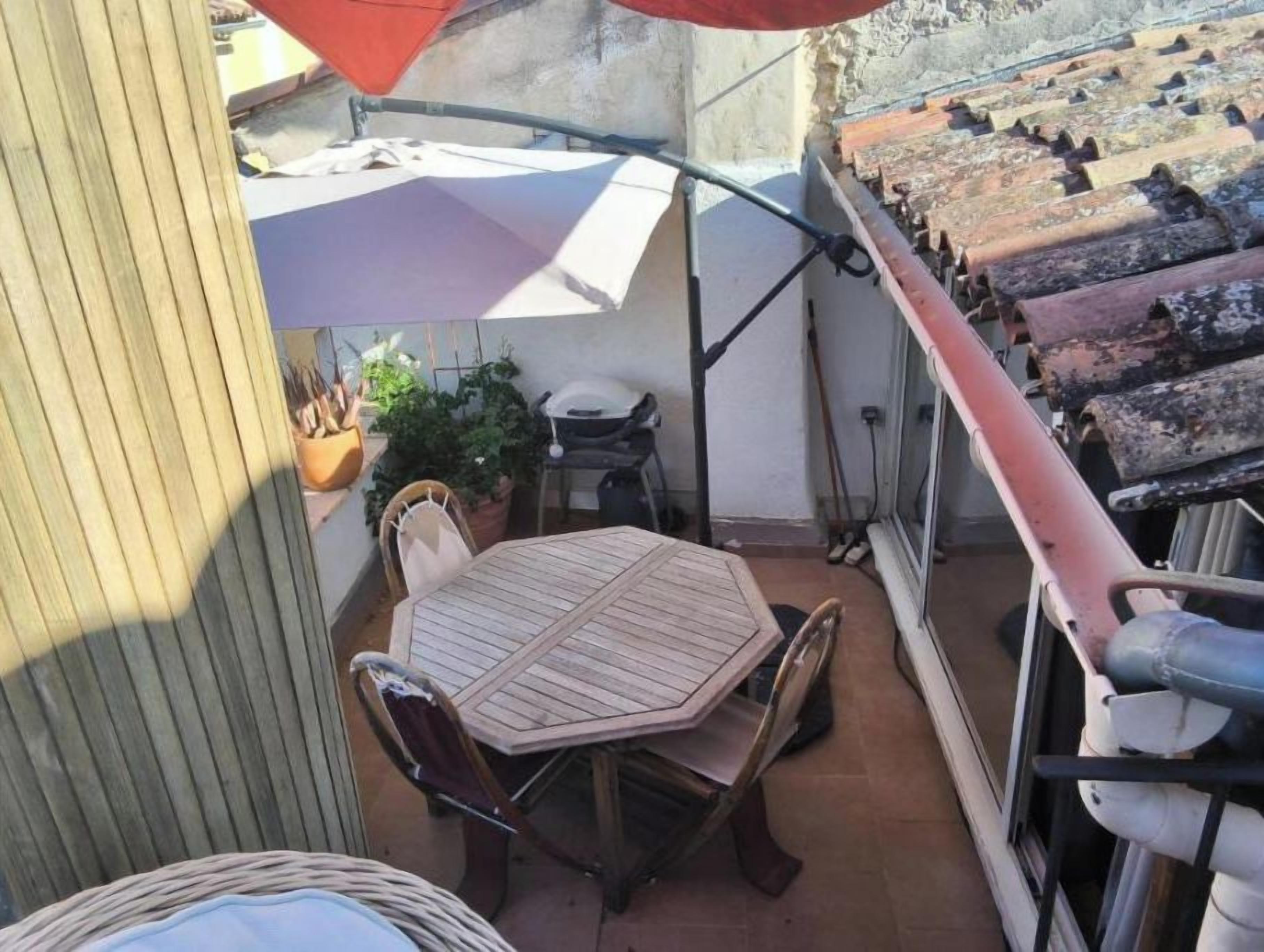 Un patio con una mesa, sillas y un paraguas rojo.