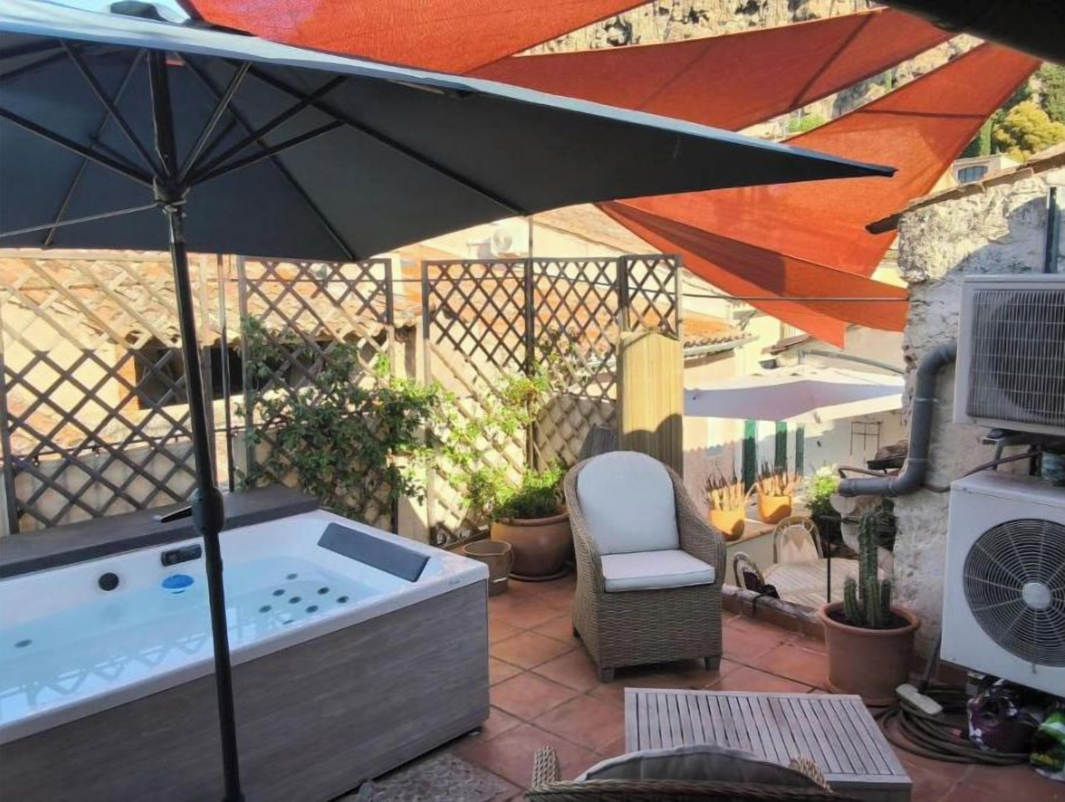 Un espace patio comprenant un jacuzzi, du mobilier d’extérieur et des parasols pour créer de l’ombre.