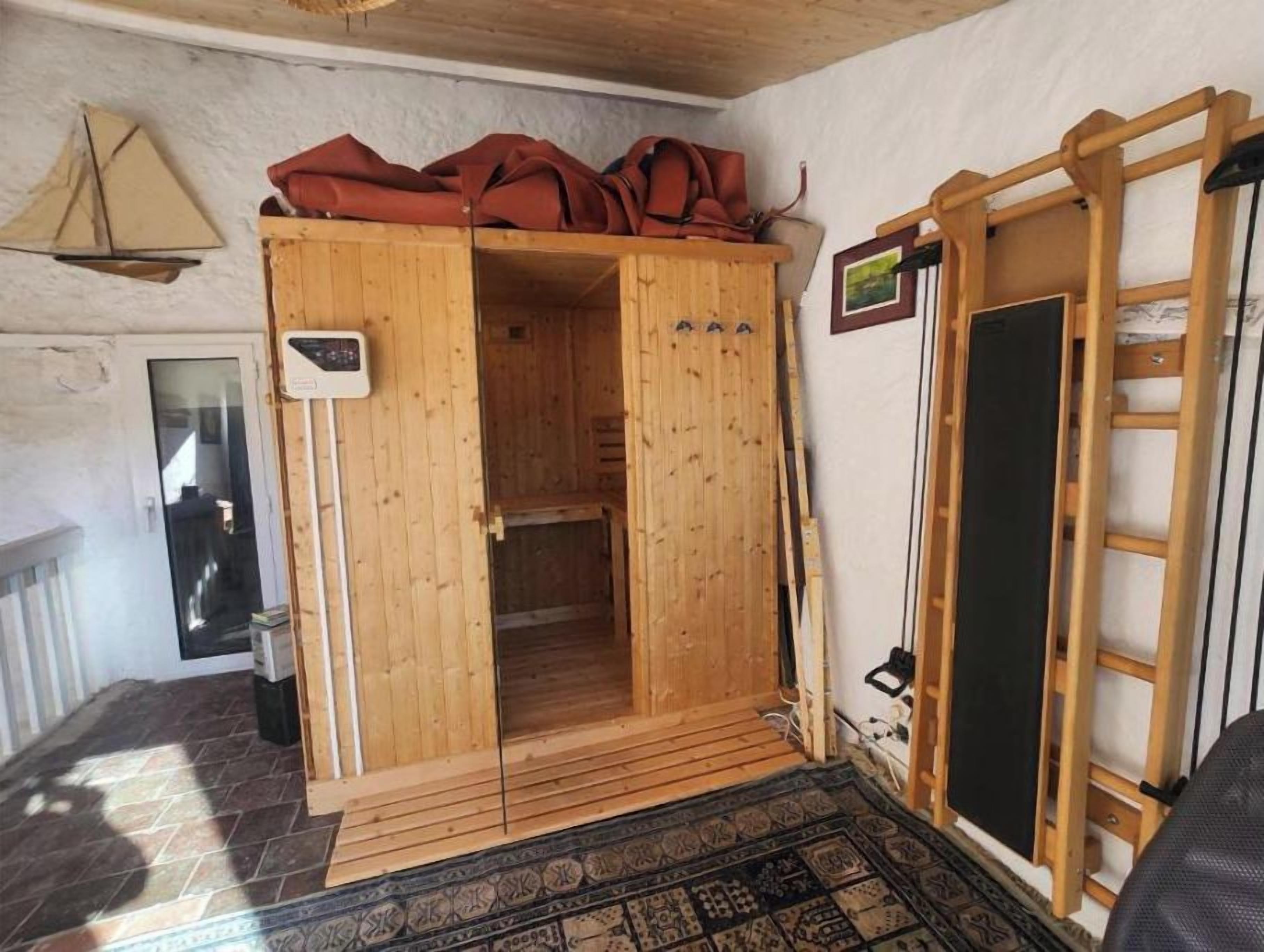 En træsauna med bænk, trædør og en lille varmeovn på væggen.