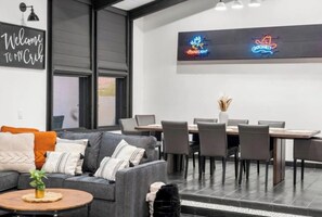 A modern interior with a grey sofa, a round coffee table, a dining table with chairs, and a neon sign on the wall.