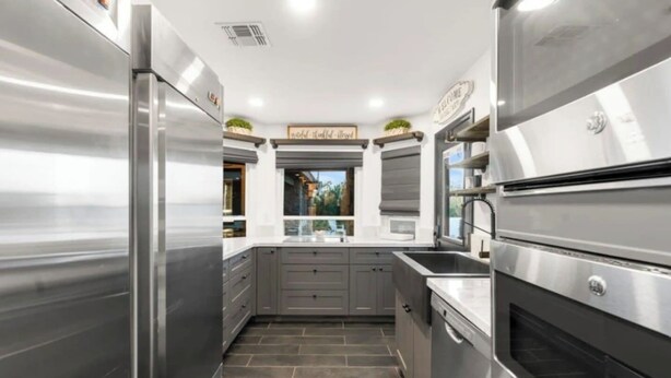 Una cocina moderna con electrodomésticos de acero inoxidable, armarios grises y vistas al exterior.