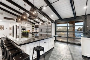 A modern kitchen with a large island, stainless steel appliances, and a view through large windows.
