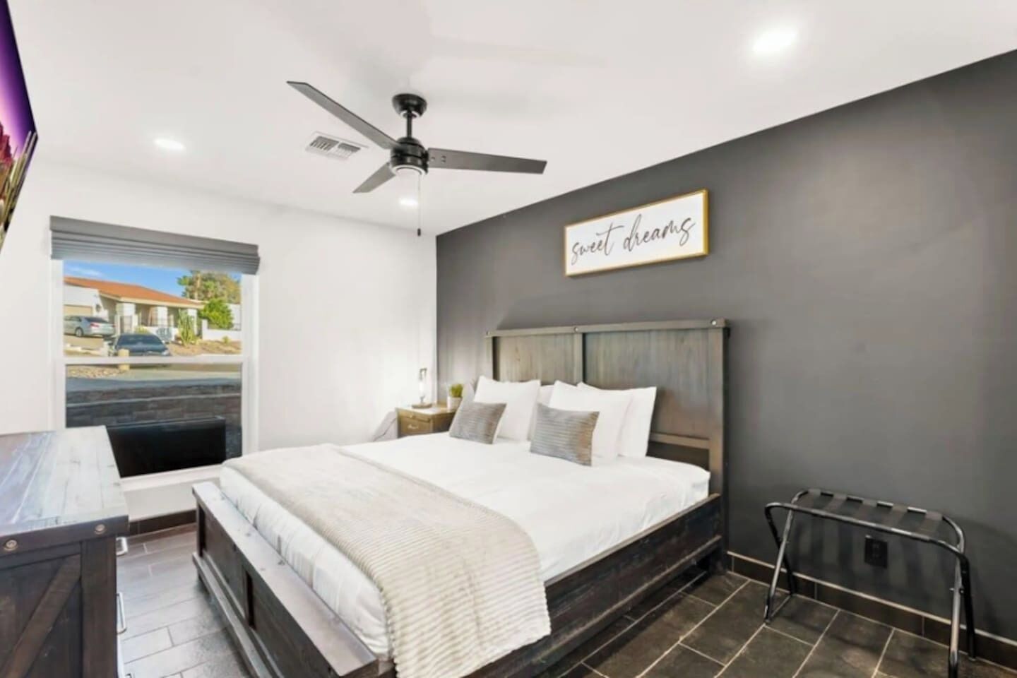 A bedroom with a bed, a ceiling fan, a window with a view, and a sign on the wall.