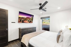 Ein Schlafzimmer mit einem Bett, einem Schminktisch, einem Deckenventilator, einem Fenster mit Ausblick und einem an der Wand befestigten Fernseher.