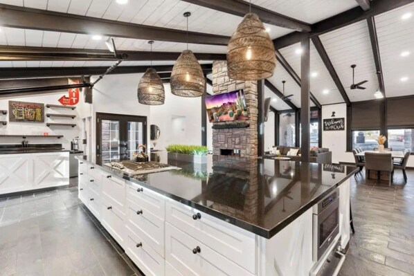 A modern kitchen with a large island, pendant lighting, and a stone fireplace.