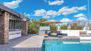 Zona de piscina con sillones de descanso, una parrilla y un patio con muro de piedra y un letrero.