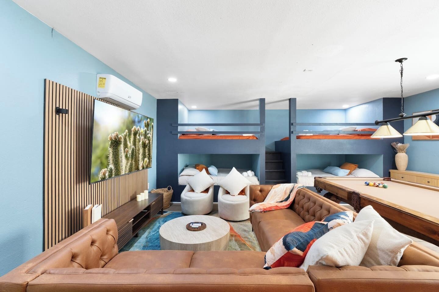 A modern living room with a sofa, armchairs, a pool table, and bunk beds.