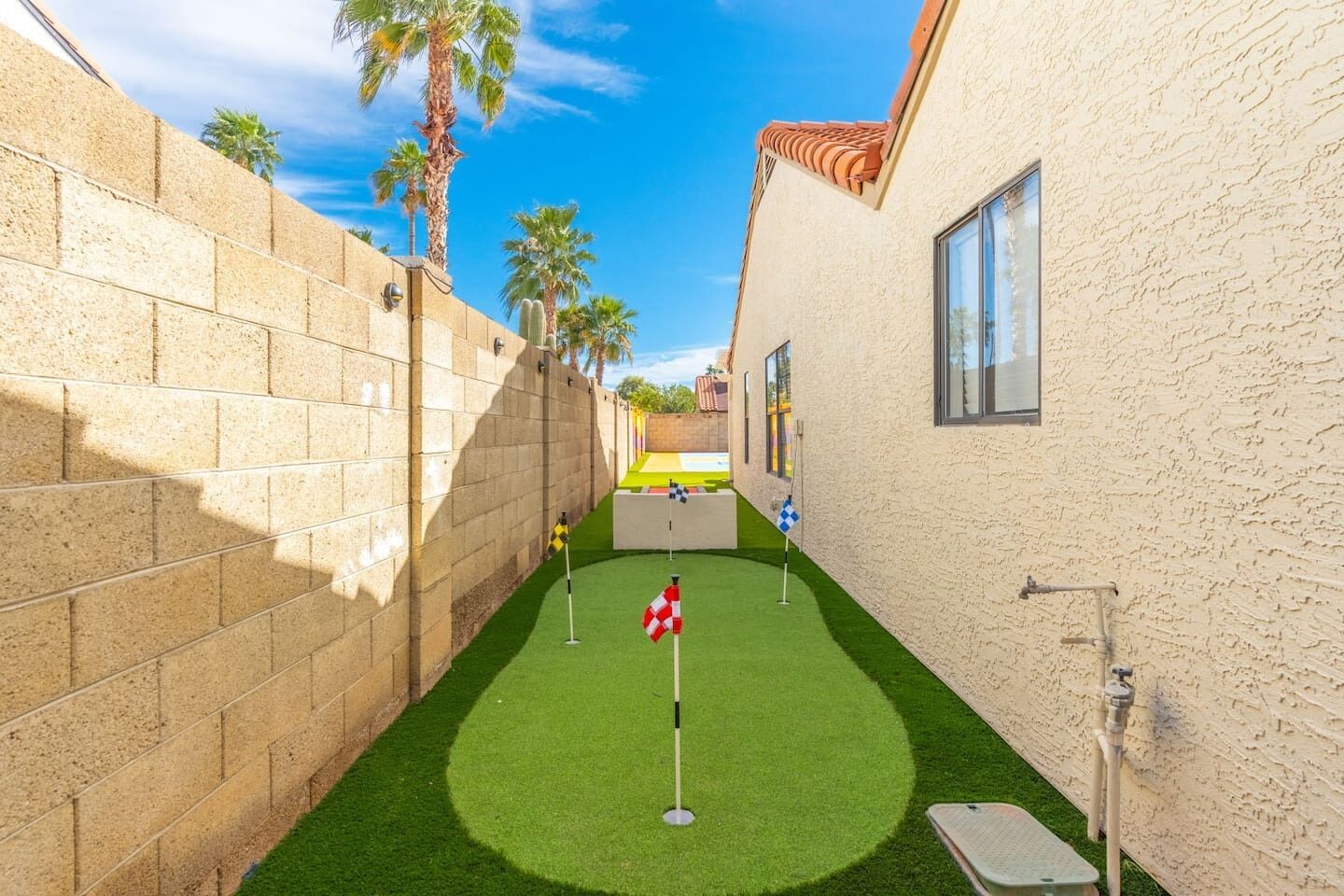 A narrow courtyard with artificial green turf, a flagpole, and a small table with a yellow object on it.