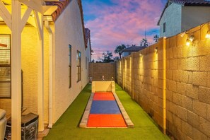 A narrow outdoor space with artificial turf, a wall with light fixtures, and a clear sky. - Heated Pool, Spa, Sauna, Mini Golf, Pickleball (Scottsdale)