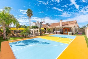 A residential area with a basketball court, outdoor seating, and a house with a tiled roof.