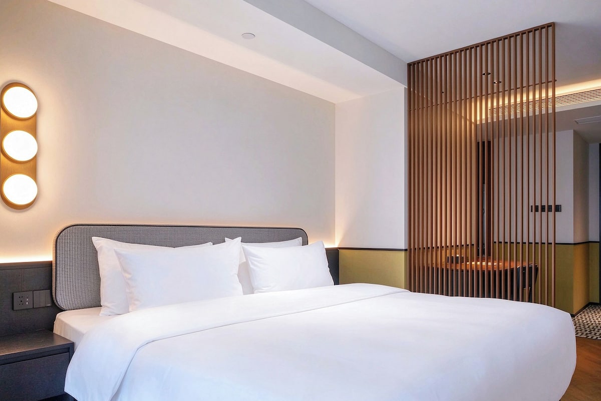 A modern hotel room with a large bed, a nightstand, and a wall-mounted light fixture.