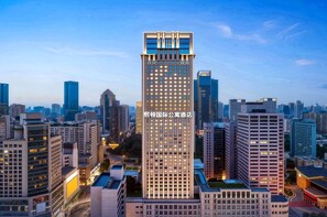 Un hotel moderno de gran altura, con varios pisos, rodeado de otros edificios altos en una vista urbana.
