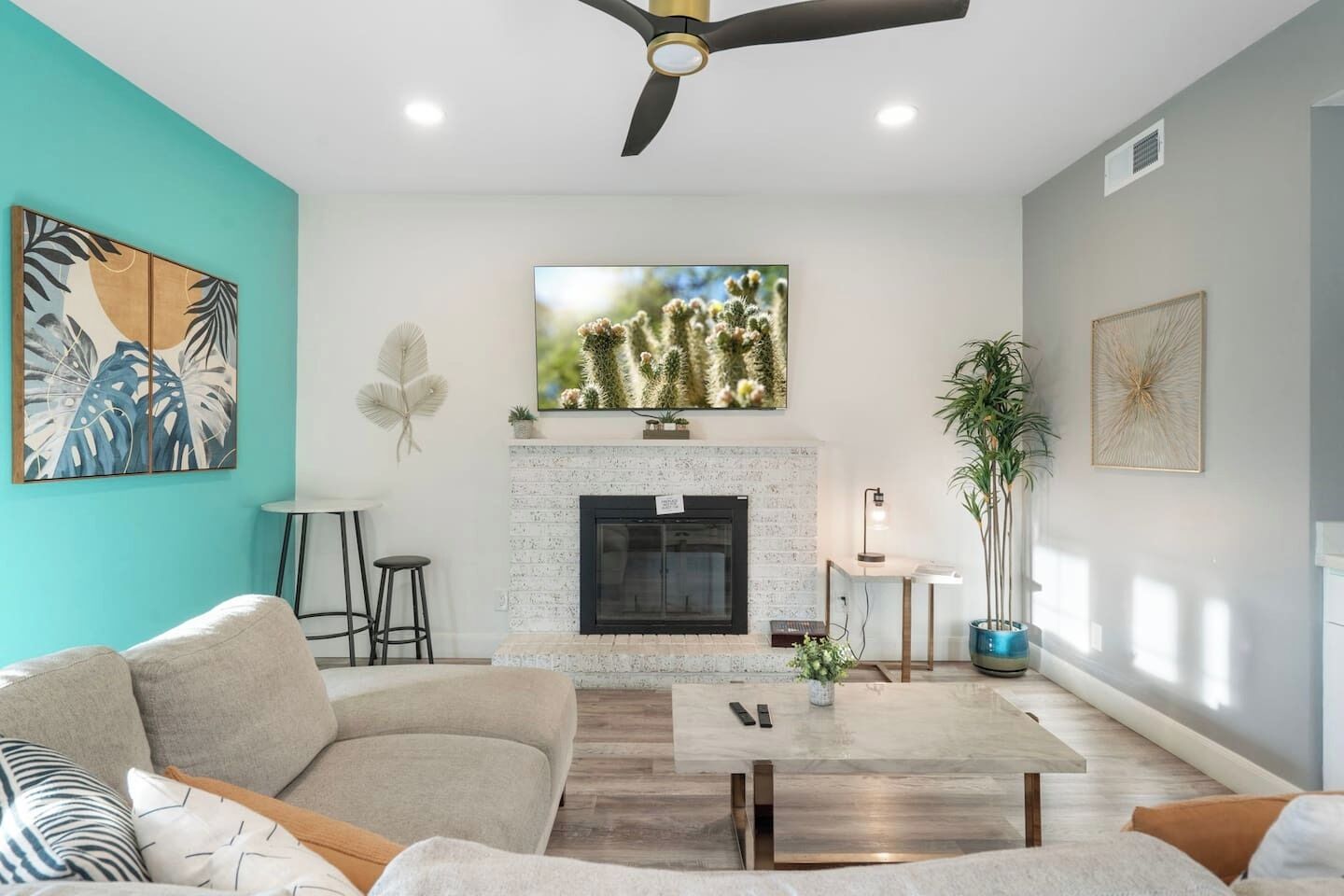 A living room with a fireplace, a ceiling fan, and a large TV mounted above it.