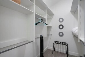 Ein weißer Kleiderschrank mit offenen Regalen, einer Kleiderstange und einem kleinen Hocker.