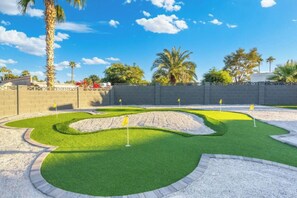 A miniature golf course with sand traps and green grass, surrounded by a brick wall and palm trees. - Ultimate Backyard | Pool, Pickleball, and Golf! (Scottsdale)