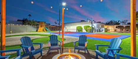 Una chimenea con sillas, una cancha de baloncesto y un parque infantil.