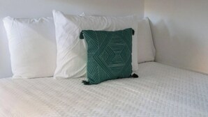 A bed with a white quilted mattress, a green patterned pillow, and two plain white pillows. - Ultimate Backyard | Pool, Pickleball, and Golf! (Scottsdale)