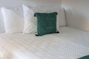 A bed with a white quilted mattress, a green patterned pillow, and two plain white pillows. - Ultimate Backyard | Pool, Pickleball, and Golf! (Scottsdale)