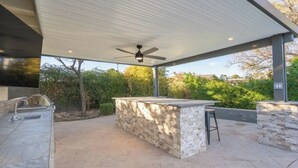 An outdoor kitchen area with a stone countertop, a built-in sink, and a ceiling fan. - Ultimate Backyard | Pool, Pickleball, and Golf! (Scottsdale)