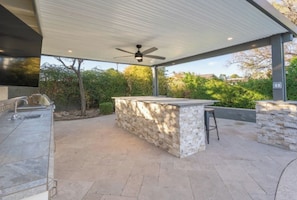 An outdoor kitchen area with a stone countertop, a built-in sink, and a ceiling fan. - Ultimate Backyard | Pool, Pickleball, and Golf! (Scottsdale)