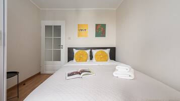 A neatly made bed with a white quilt, two pillows with yellow accents, and a book on the bed.