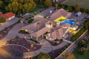 Ein großes, mehrgeschossiges Haus mit Schwimmbad, umgeben von angelegten Gärten und einer Auffahrt.