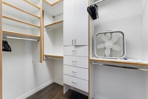 Ein begehbarer Kleiderschrank mit offenen Regalen, einem Spiegelkleiderschrank und einem weißen Ventilator auf einem Regal.