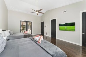 Ein Hotelzimmer mit zwei Betten, einem Deckenventilator, einem an der Wand befestigten Fernseher und einer Tür zu einem Balkon.