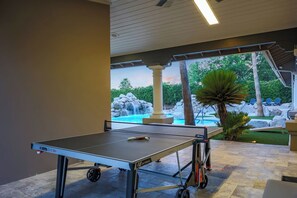 A ping pong table with a net, positioned in an outdoor area with a pool and palm trees in the background.